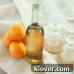 Liter bottle of Orangecello with 4 oranges and two glasses beside the bottle.