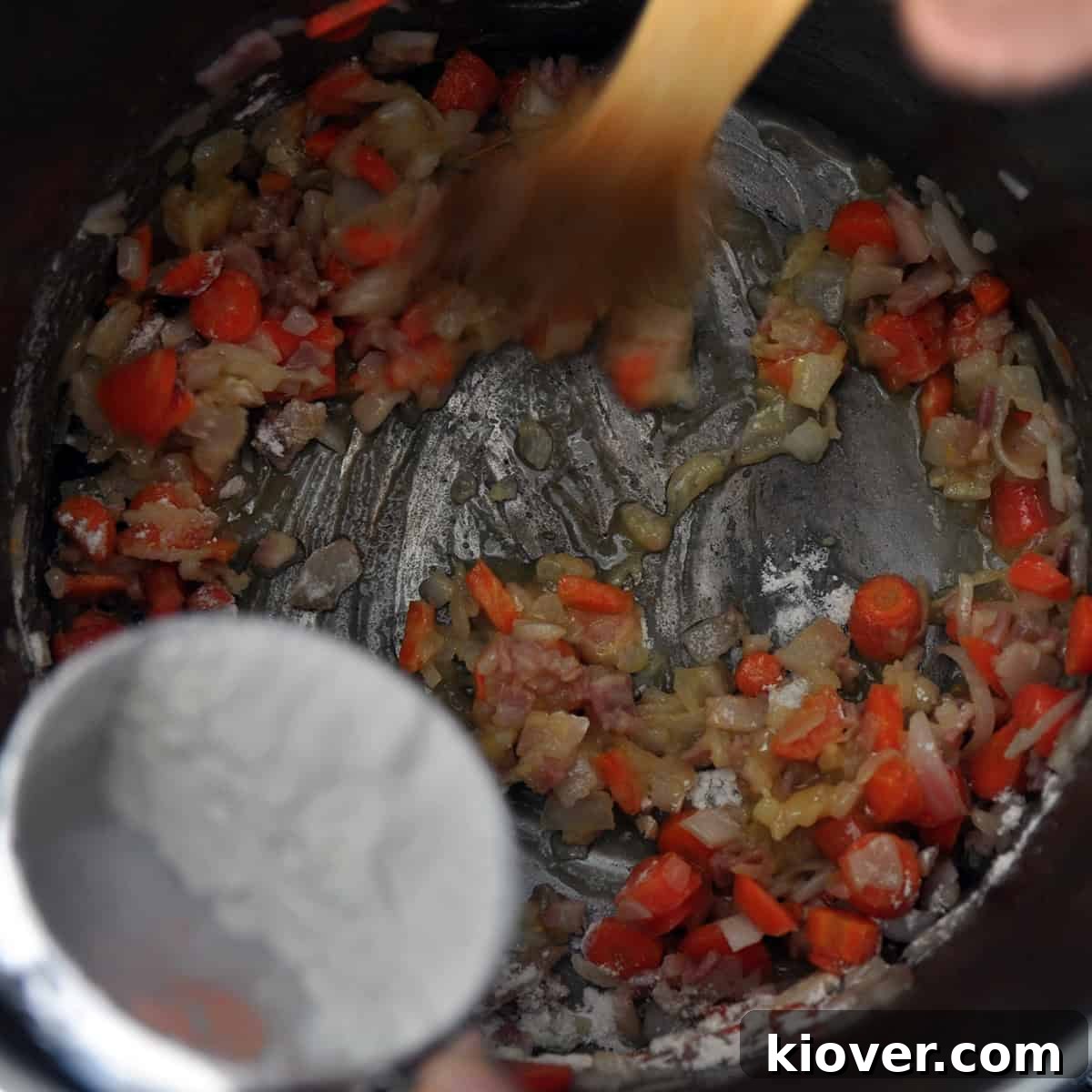 A container pouring flour into a pot of cooking vegetables.
