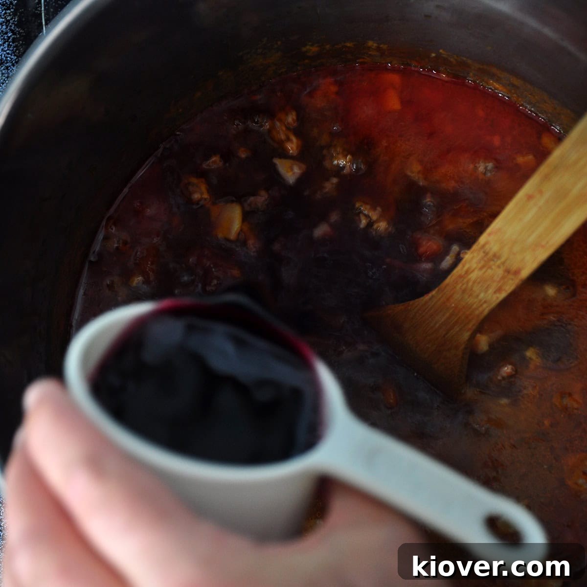 Pouring a red wine into the sauce.