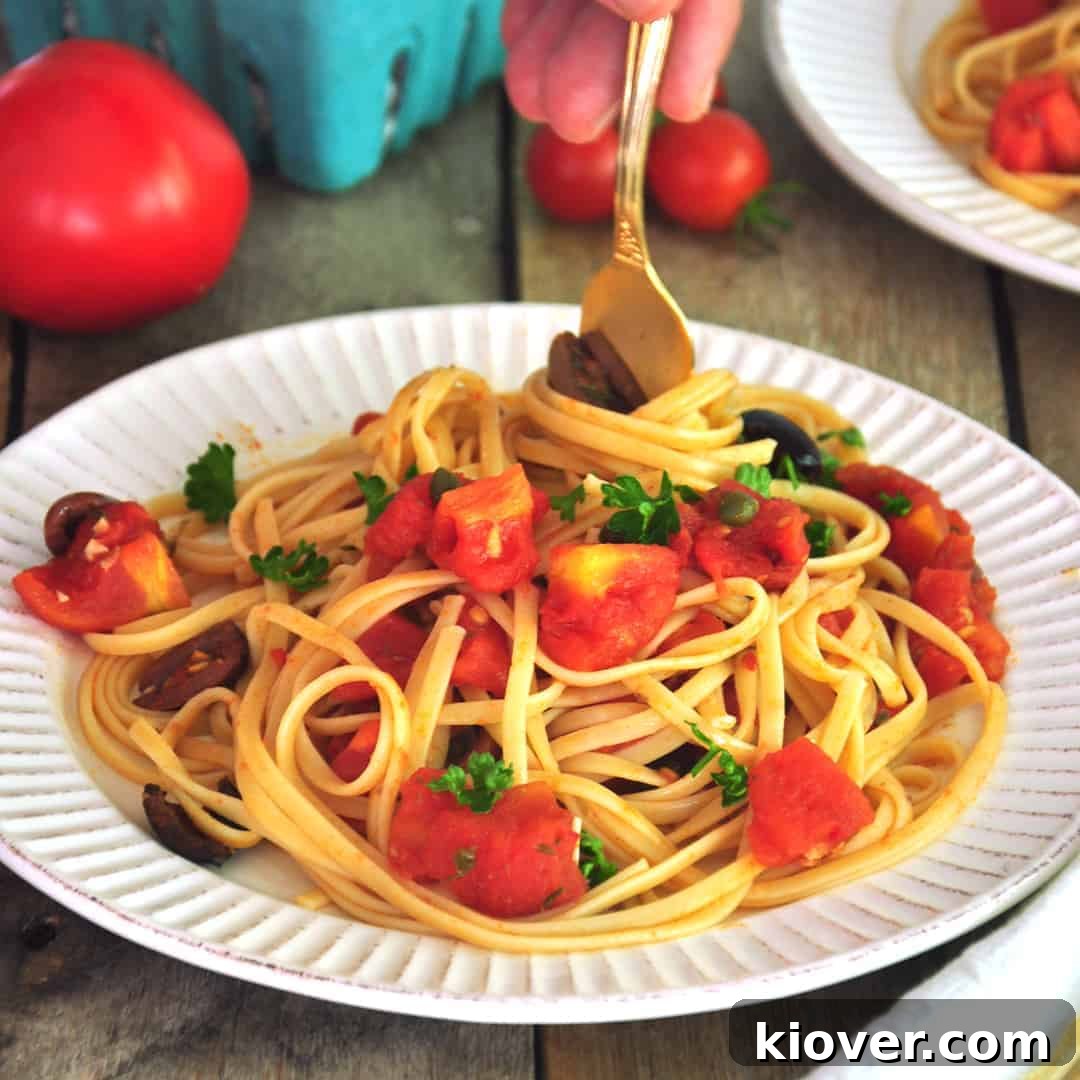 Twirling linguine and Puttanesca sauce around gold fork and getting ready to eat, a close-up of the delicious dish.