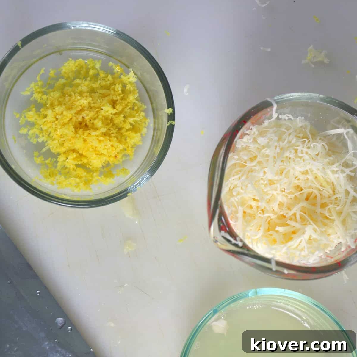Containers holding fresh lemon zest, lemon juice, and grated Parmesan cheese, highlighting simple yet quality ingredients.