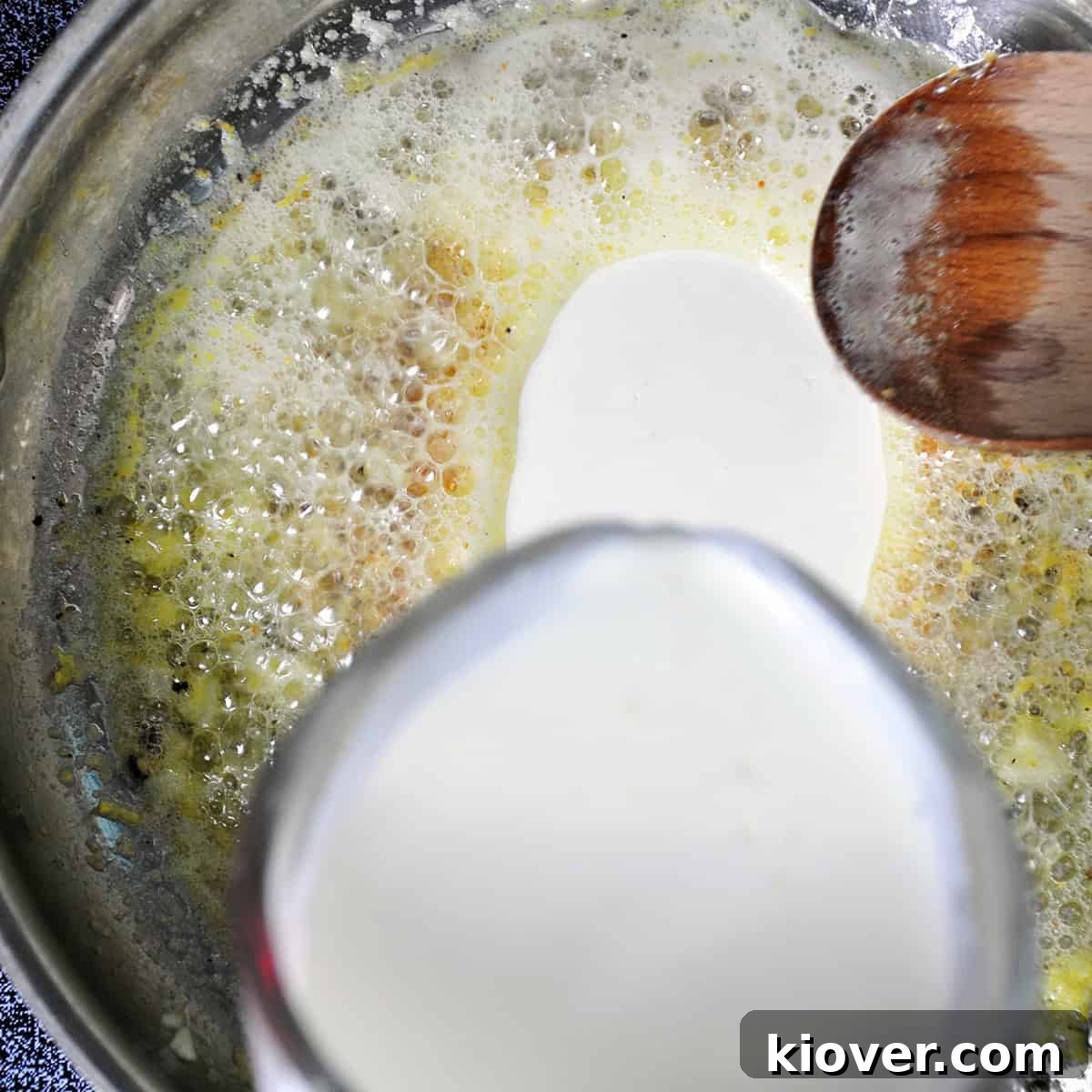 Thick heavy cream being poured into the simmering lemon butter sauce in a pan, creating a creamy base.