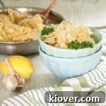 Creamy Lemon Pasta over Farfalle in a light blue bowl, with the full skillet dish shown behind it.