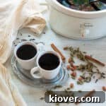 Two cozy mugs of Glogg, a Scandinavian mulled wine, on a white tablecloth, surrounded by festive spices and holiday decorations.