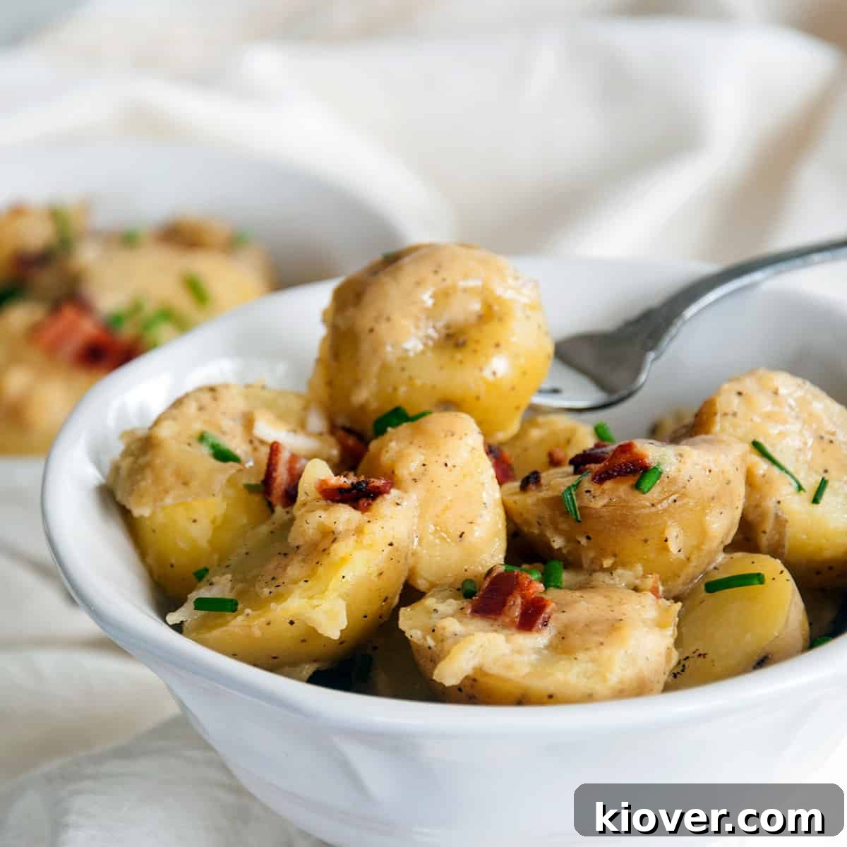 A beautifully presented bowl of warm German potato salad (Kartoffelsalat), garnished with fresh chives and crispy bacon bits, with a fork gently placed, ready to be served.