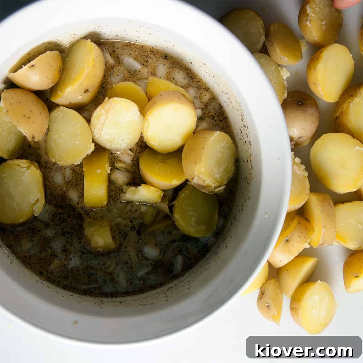Warm, neatly cut potato chunks being gently tossed into a bowl with the tangy vinegar dressing, ensuring every piece is coated.