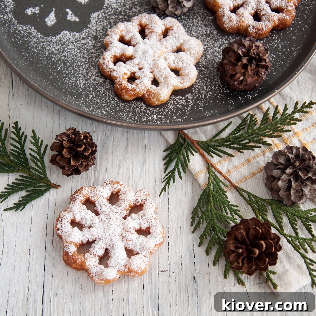 Crispy Nordic Rosette Cookies 2 A beautifully fried rosette cookie, golden brown and lightly dusted with powdered sugar, resting on a white plate with festive pinecones and evergreen branches in the background, hinting at its Christmas tradition.