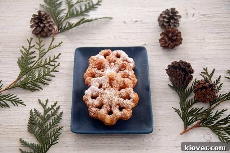 Rosette Cookies Three golden Rosette Cookies, beautifully shaped and dusted with powdered sugar, arranged on a square blue plate, with subtle holiday decorations in the background creating a festive ambiance.