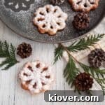 A close-up image of two perfectly golden-brown Scandinavian Rosette Cookies, intricately shaped and delicately coated with powdered sugar, against a warm, inviting background, highlighting their traditional charm.