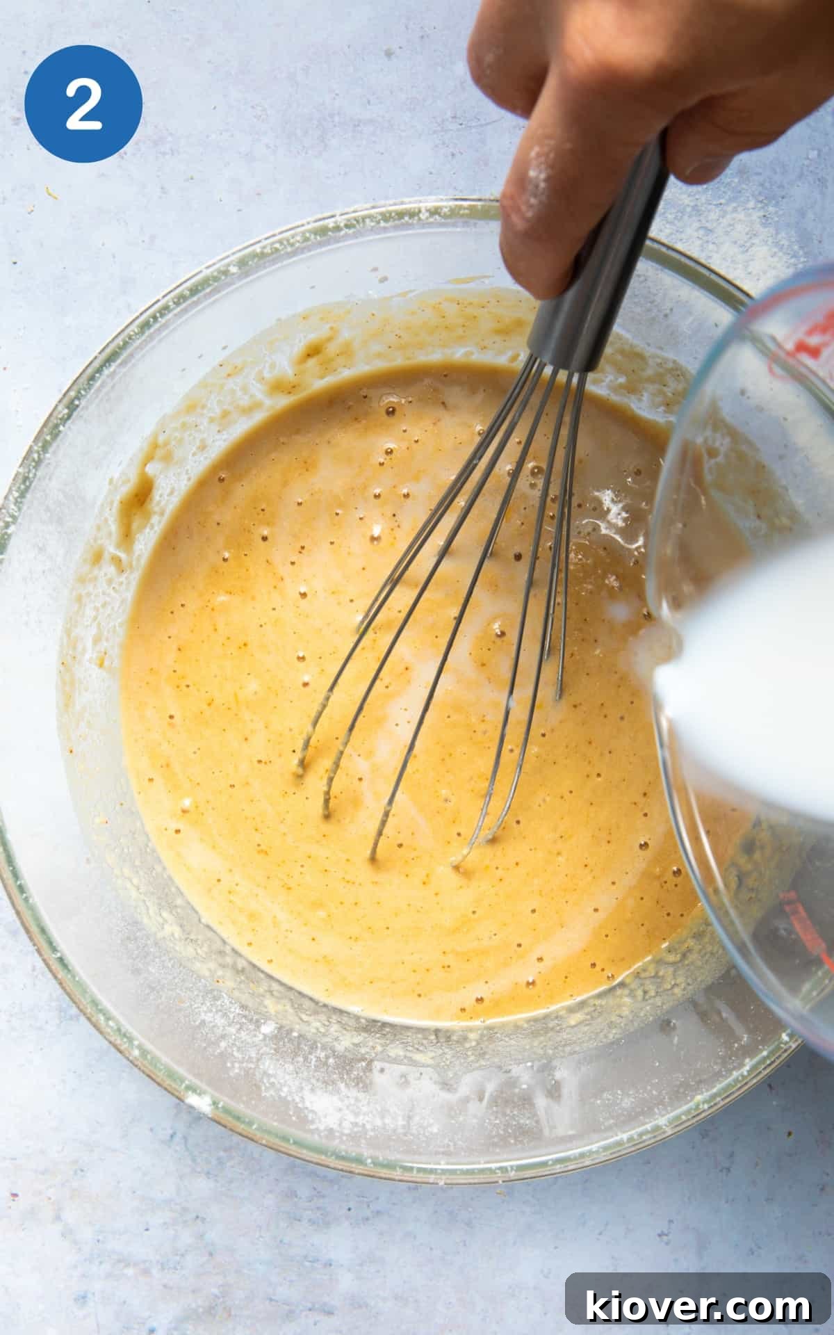 The lemon drizzle cake batter being gently mixed in a large bowl with a whisk, showcasing its smooth consistency and flecks of lemon zest.