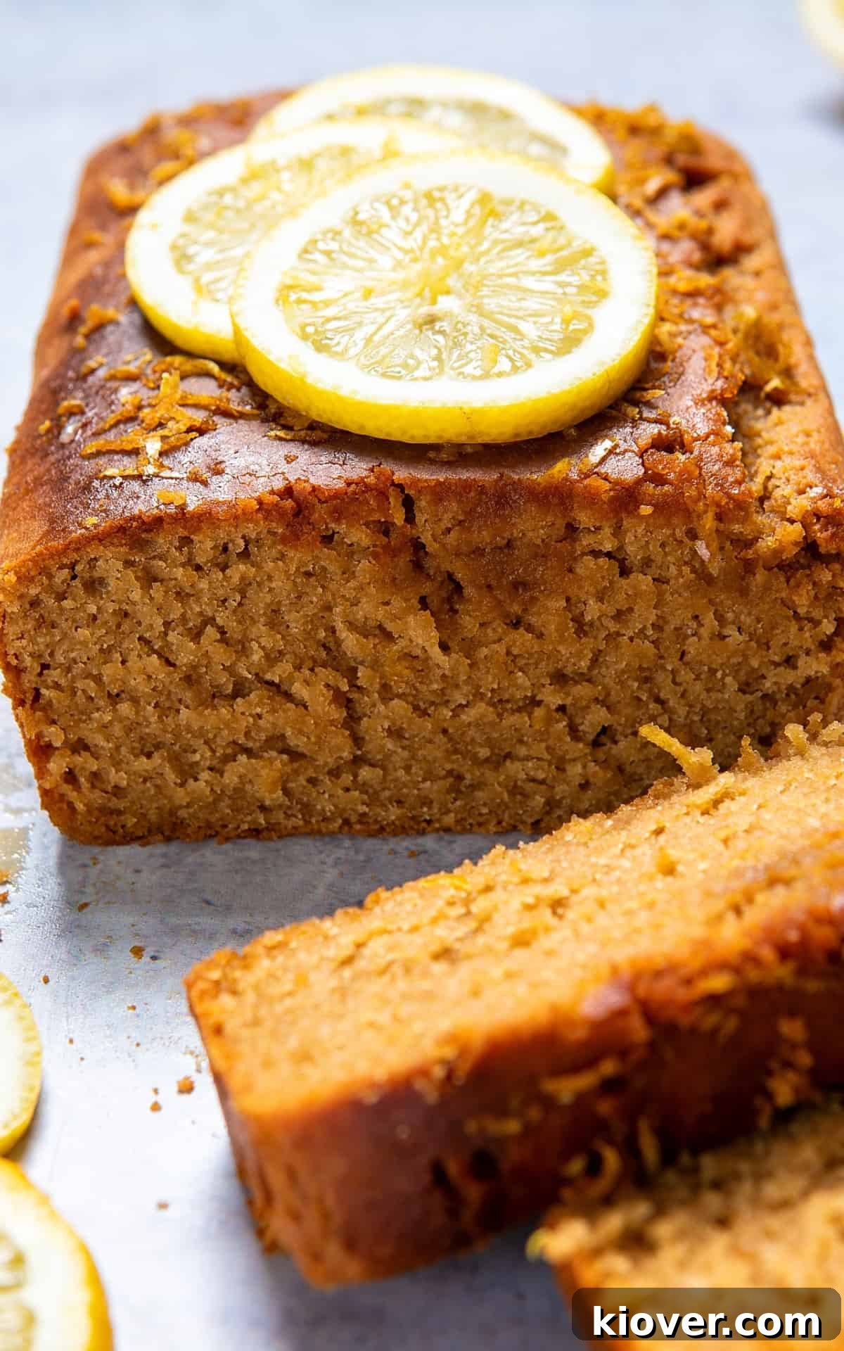 A cross-section of the vegan lemon drizzle cake, revealing its moist crumb and topped with delicate lemon zest and slices.