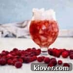 Purple Haze Cocktail on a white table with cranberries around the glas.