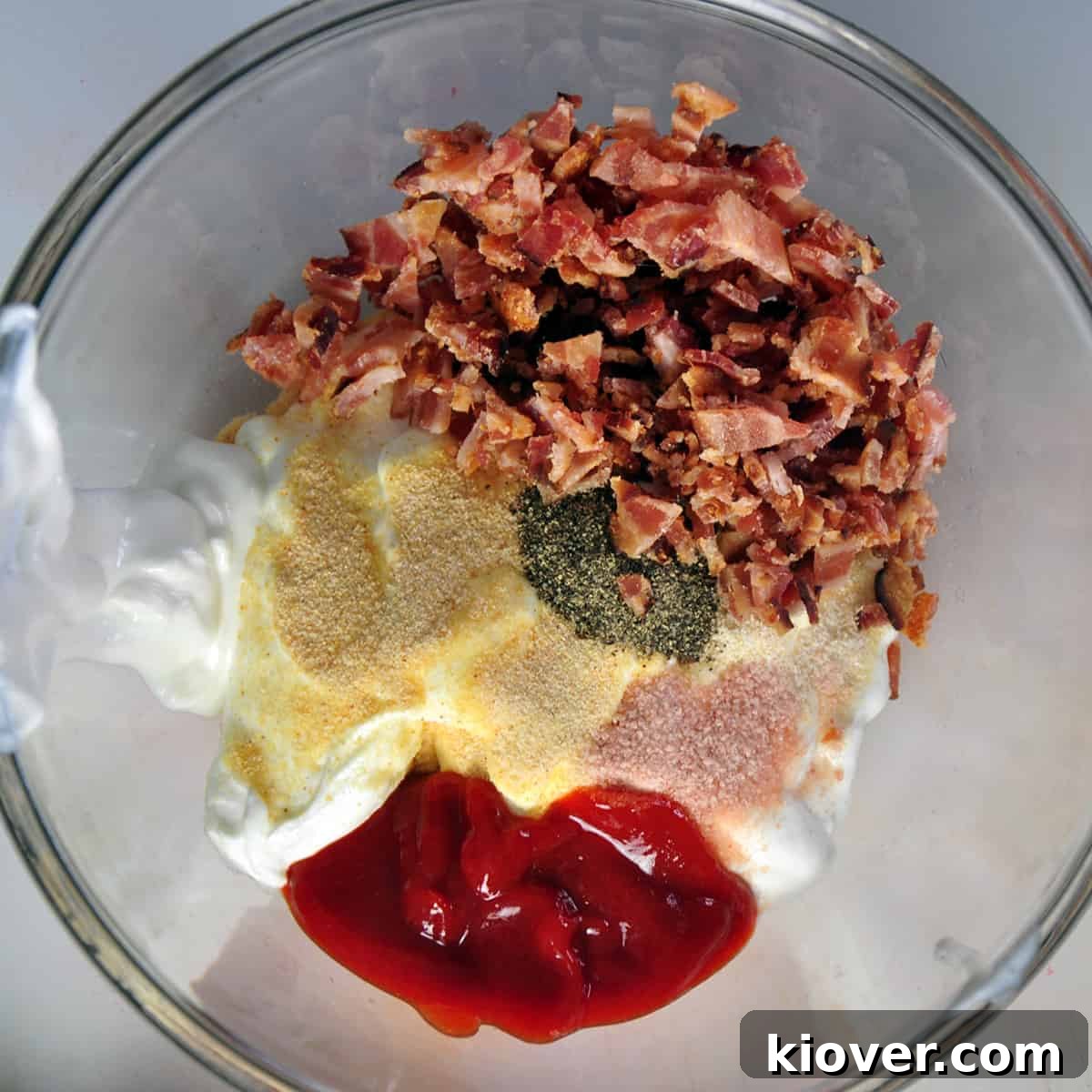Chip dip ingredients A vibrant display of all the chip dip ingredients laid out in a pristine white bowl, ready for mixing. The rich red of Sriracha contrasts beautifully with the creamy white of sour cream, alongside the earthy tones of spices and the crispy texture of bacon bits.