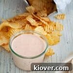 A small square image of the Bacon and Sriracha Chip Dip, garnished with a swirl of Sriracha and crispy bacon bits, ready to be served.