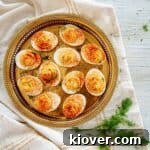 A top-down view of Dill Pickle Spicy Deviled Eggs, garnished with paprika and a sprig of dill, served on a round gold platter.