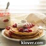 Stack of Swedish Pancakes Recipe on a white plate with Lingonberry jam, whipped cream, and powdered sugar on top.