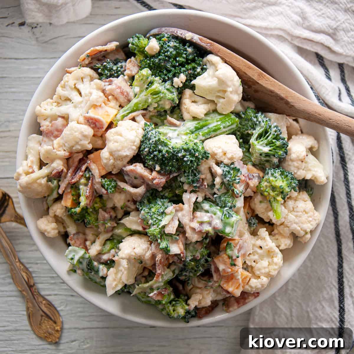 A beautifully presented Extra Baconey Amish Broccoli Salad in a white bowl, ready to be served with a wooden spoon.
