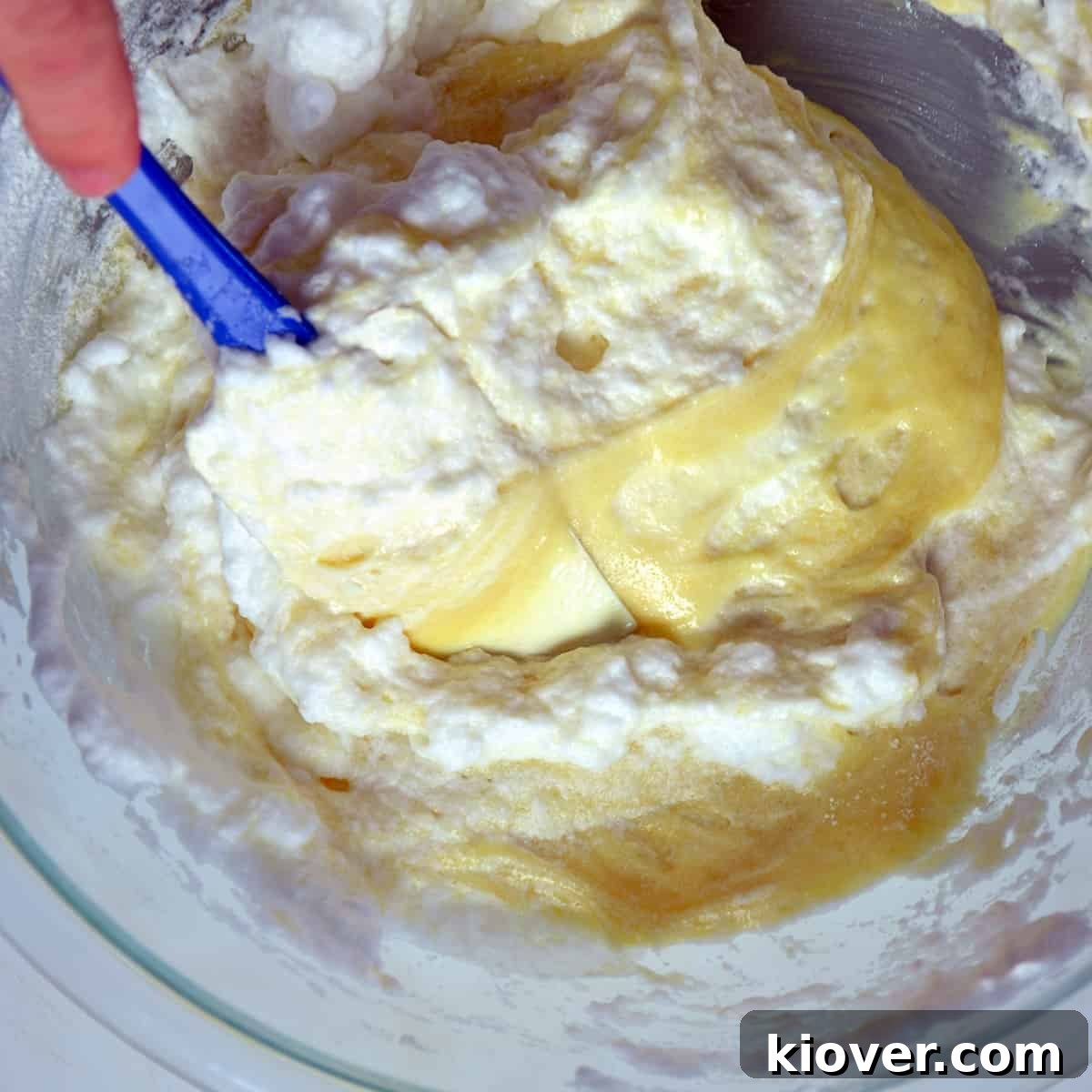 Mixed Batter Cake batter and egg whites gently mixing with a rubber spatula in a large glass bowl.
