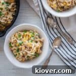 Two white bowls filled with Homemade Skillet Tuna Helper and two silver spoons on a white and blue cloth.