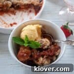 One serving of Strawberry Rhubarb Cobbler with a side of vanilla ice cream and garnished with a few leaves of mint. This is served in a white bowl with a silver spoon.