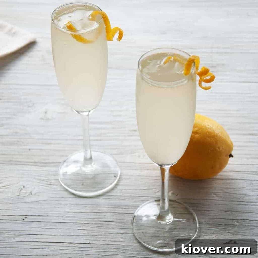 Two French 76 Cocktails on a white table with lemon peel garnish and a whole lemon in the background.