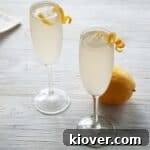 Two French 76 Cocktails on a white table with lemon peel garnish and a whole lemon in the background.