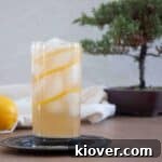 A single Horse's Neck Cocktail on a serving plate with a lemon and bonsai tree in the background.