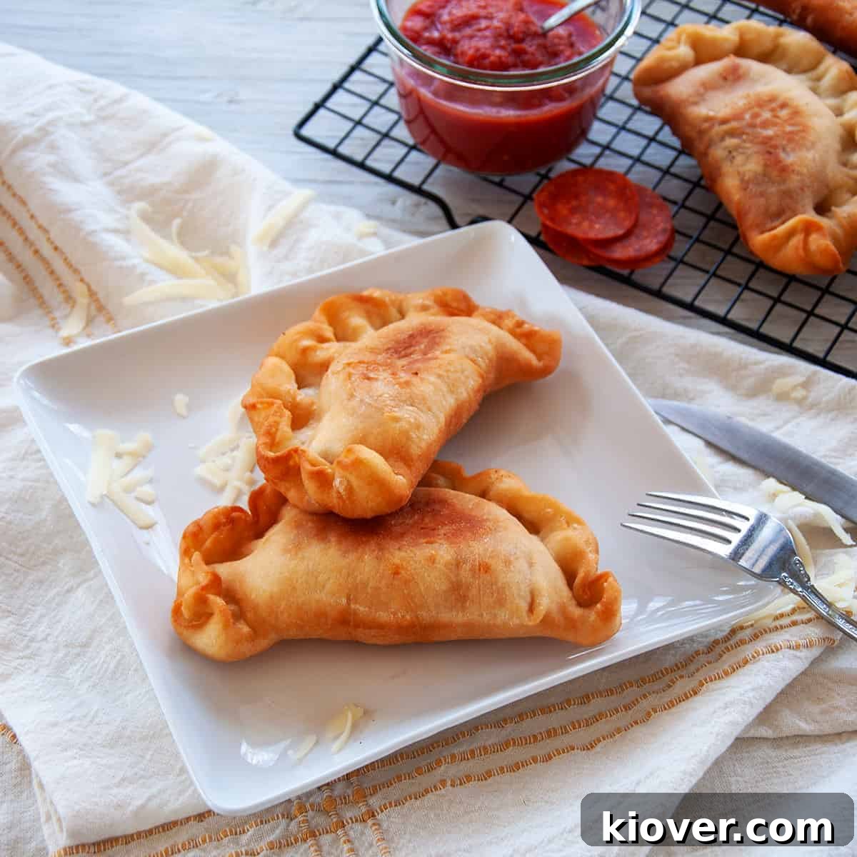 Two golden-brown, crispy fried Italian Panzerotti resting on a pristine white plate, accompanied by a fork on the side, showcasing their delectable texture.