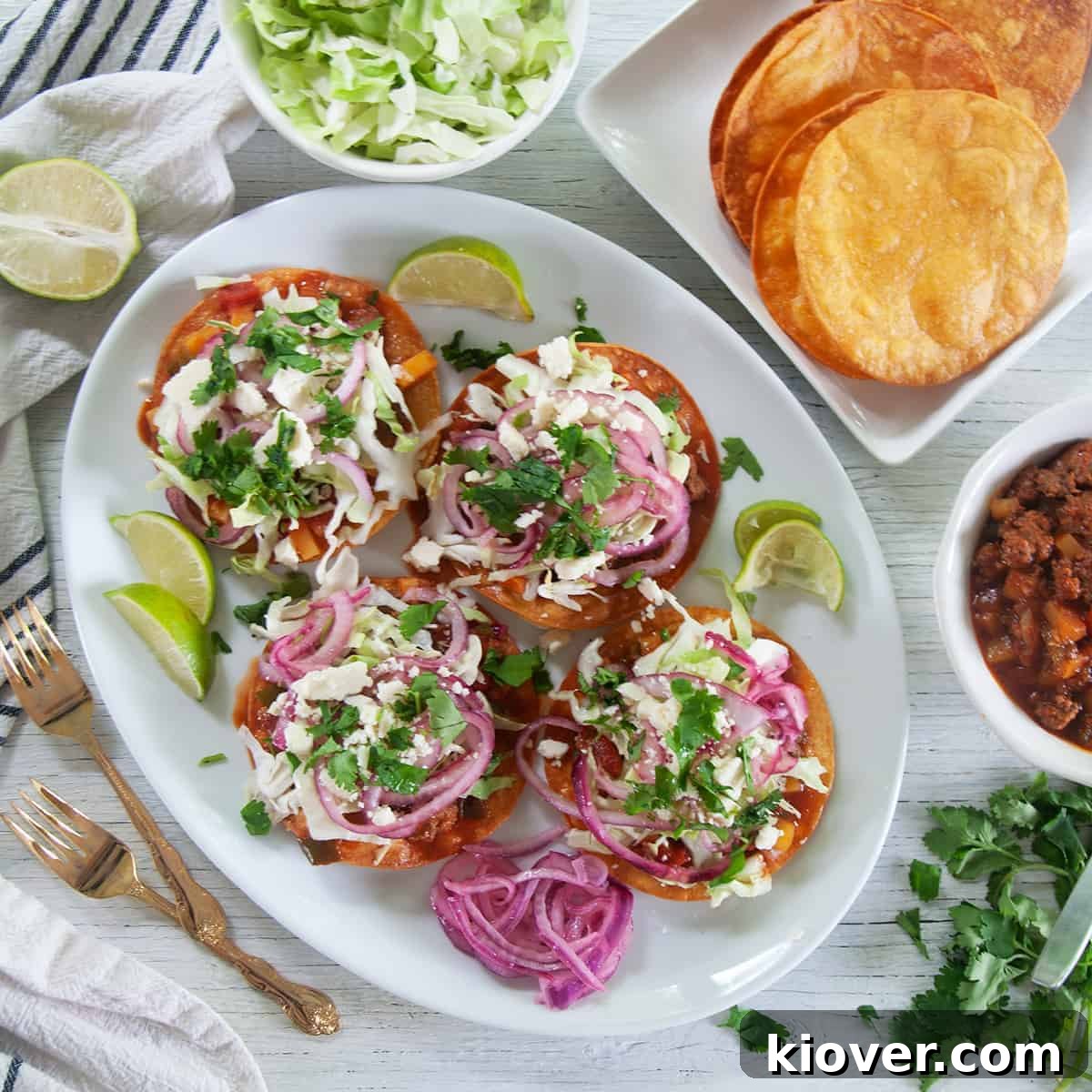 Four Honduran Enchiladas on top of a large white plate with red onions on the side, limes, and two gold forks.