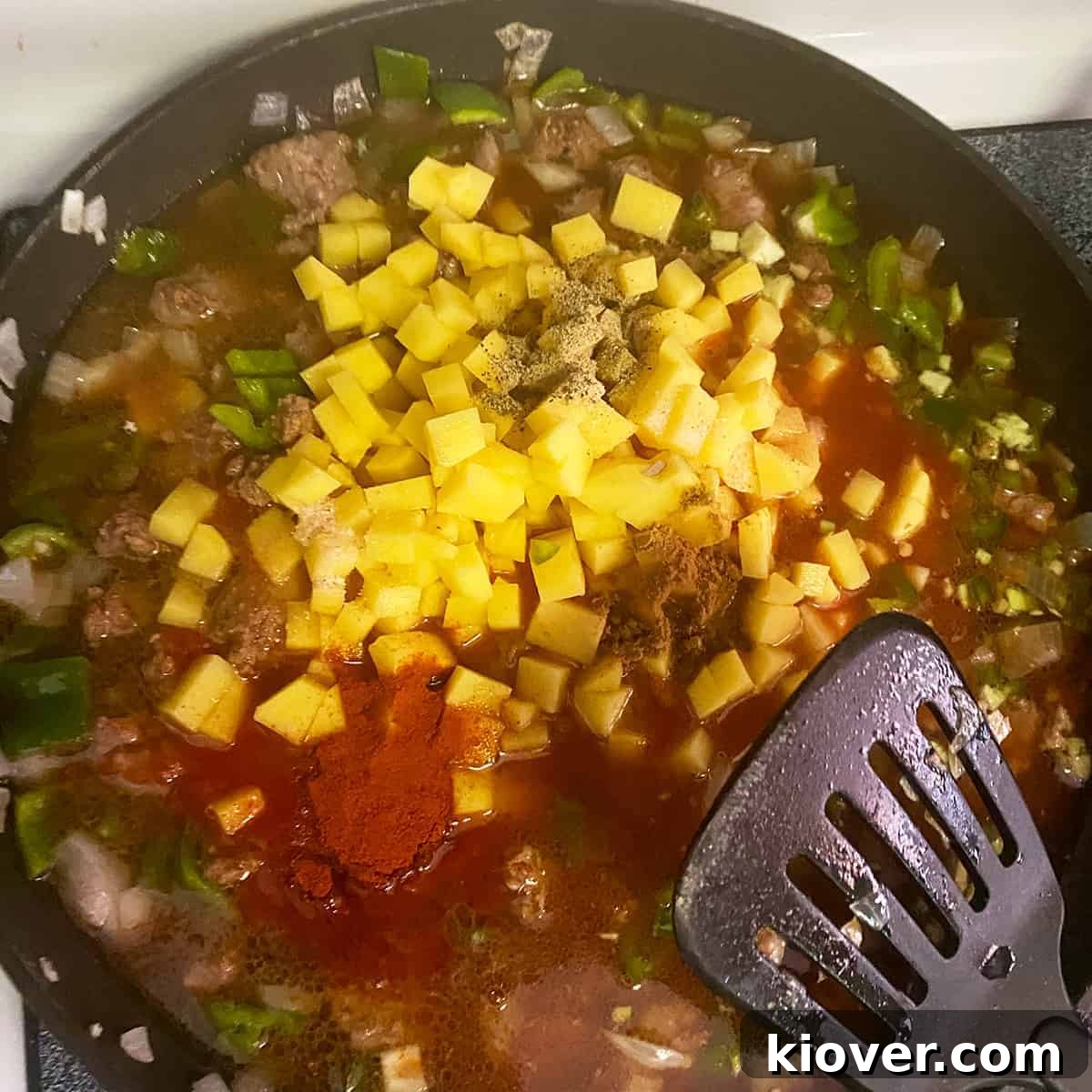 All filling ingredients added to a pan being brought to a simmering temperature and a spatula sitting on the side.