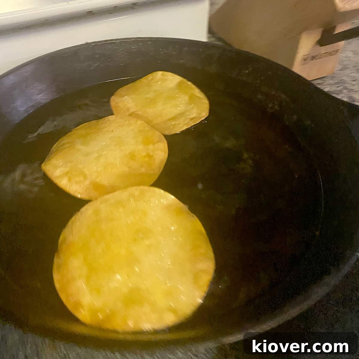 Three corn tortillas frying in hot oil in a cast iron pan.