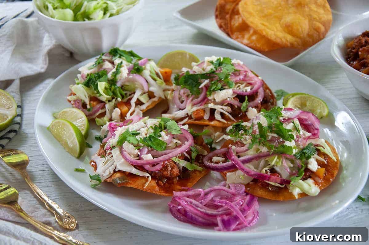 A big white platter full of Honduran Enchiladas, red pickled onions, and limes on the side.