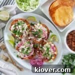 Four Honduran Enchiladas on top of a large white plate with red onions on the side, limes, and two gold forks.