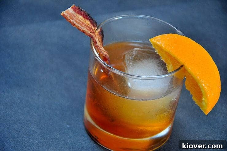 Close-up of a Bacon Bourbon Maple Old Fashioned garnished with a crispy bacon strip and an orange twist, highlighting the rich colors of the cocktail.