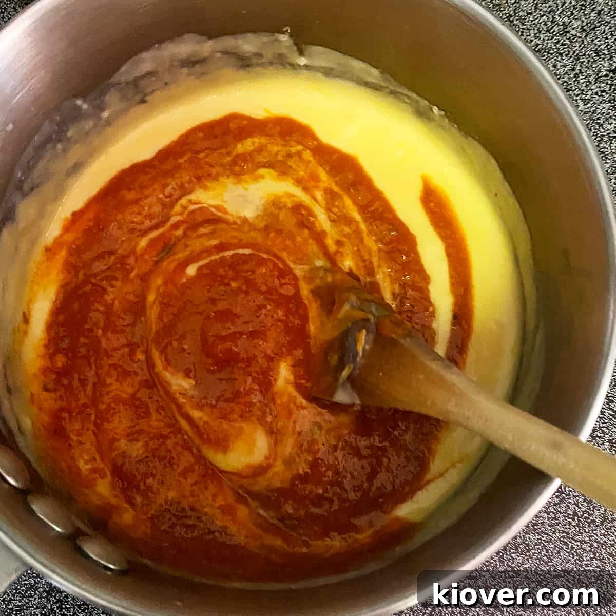 Effortless Creamy Homemade Queso 3 Cheese and salsa being mixed in a saucepan over heat, with a wooden spoon stirring the concoction.