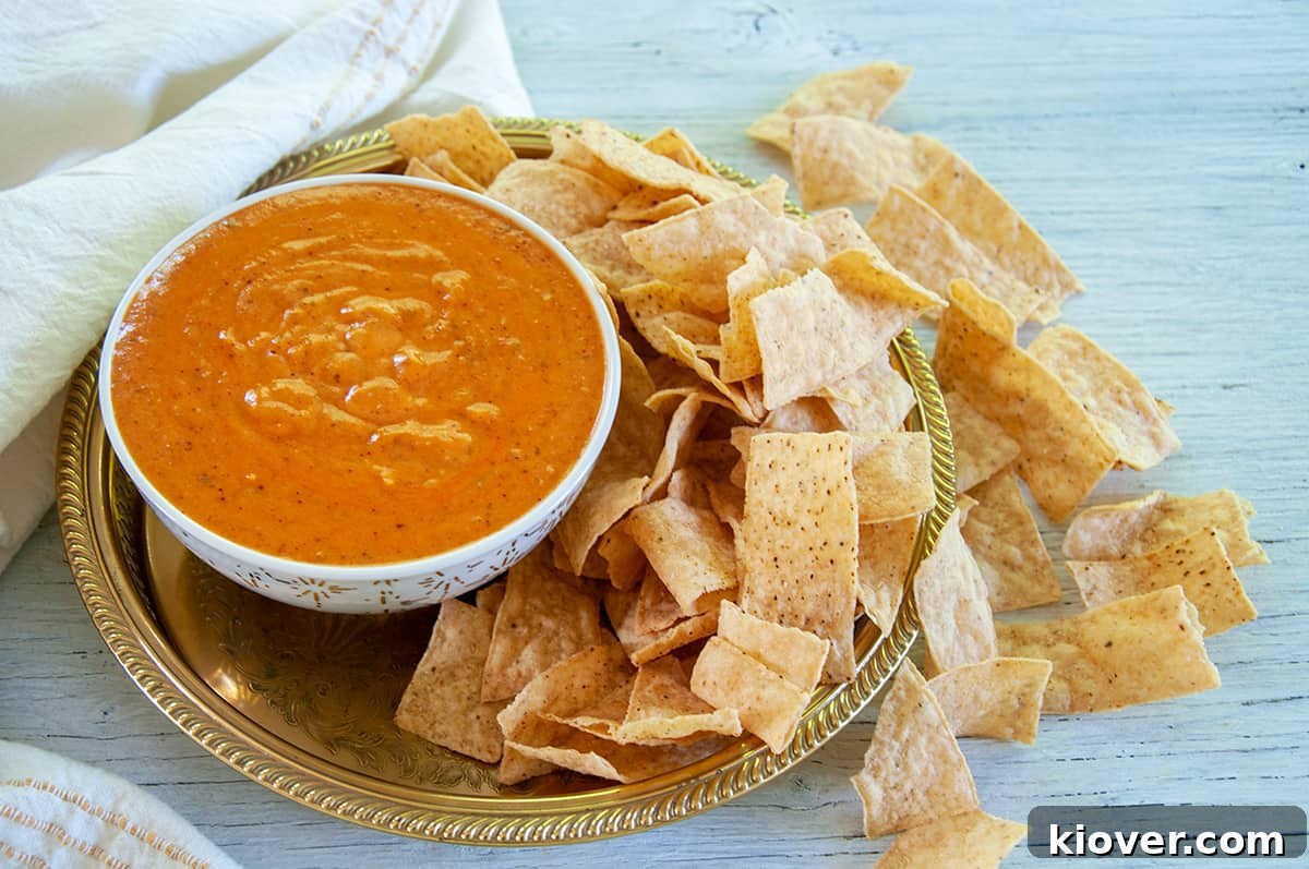 Homemade Queso Dip Bowl of queso dip on a gold platter with corn chips spread all around the platter and the table underneath.