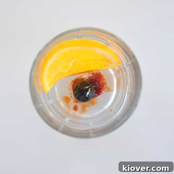 Old Fashioned Fruits Ready Lemon peel, a vibrant red cherry, bitters, and sugar at the bottom of a glass, preparing for the muddle.