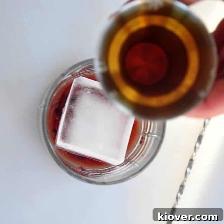 Pour Whisky into Old Fashioned A hand pouring whiskey into a glass containing the muddled ingredients for an Old Fashioned cocktail.