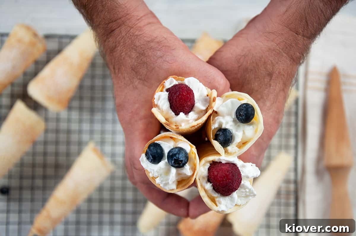 Holding four krumkakke in my hands over a cooling tray of unfilled krumkakke cones.