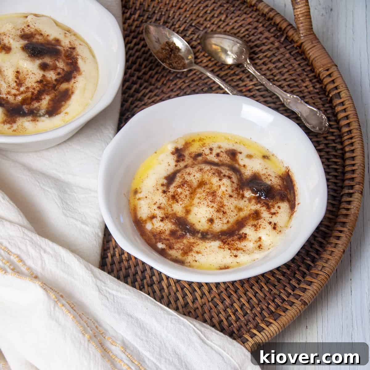 A bowl of creamy Rømmegrøt, garnished with cinnamon and melted butter, resting on a wicker platter beside a white linen cloth, evoking a sense of rustic elegance and comfort.