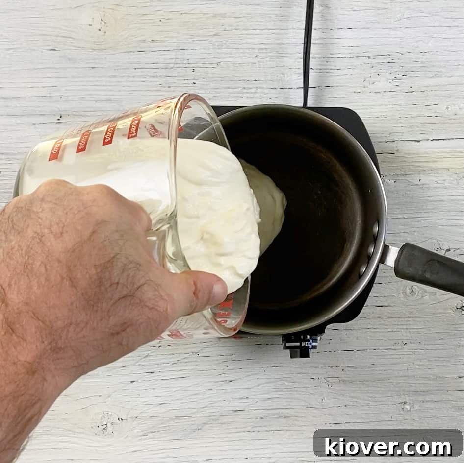 Thick, rich homemade sour cream being carefully poured into a gleaming saucepan, demonstrating the ideal consistency for crafting authentic Rømmegrøt.