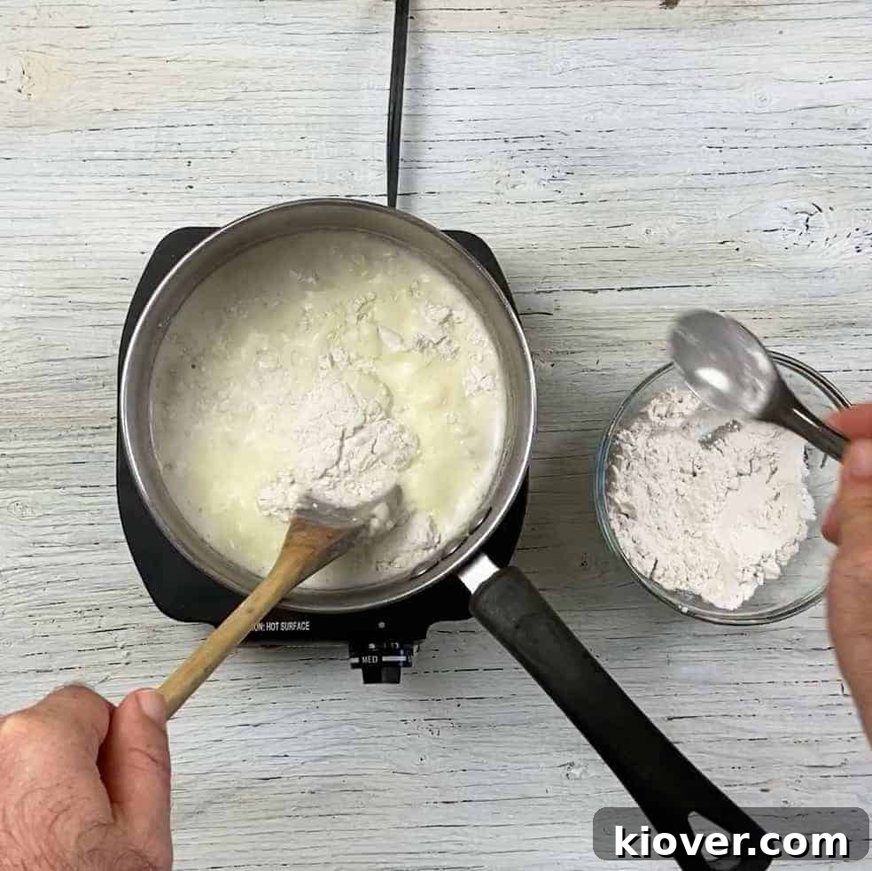 Finely milled flour being gradually whisked into simmering sour cream in a pot, illustrating a key step in creating the smooth, creamy base of Rømmegrøt.