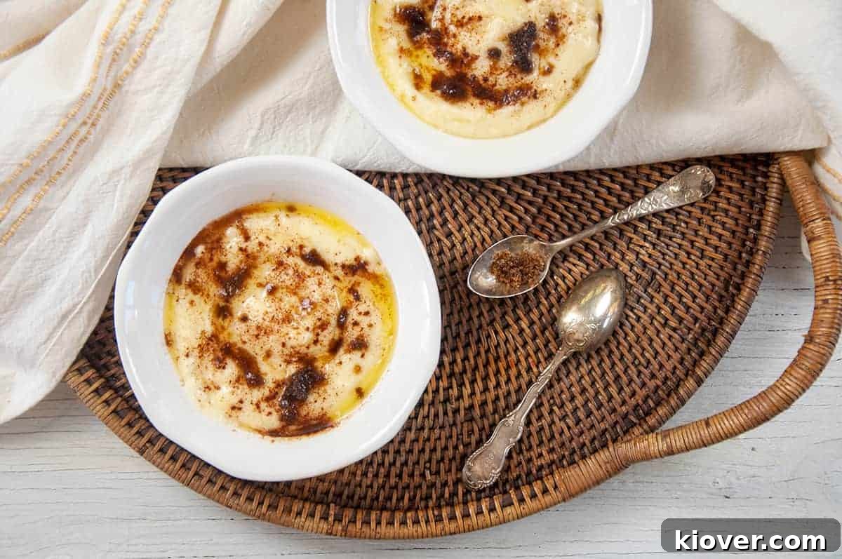 Two white bowls filled with Rømmegrøt, adorned with cinnamon and melted butter, are elegantly arranged on a rustic wicker platter, accompanied by antique silver spoons.