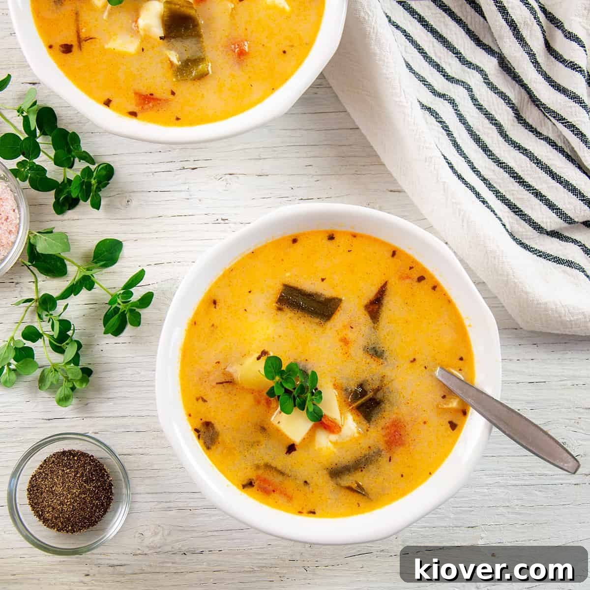 Two bowls of Caldo de Queso with oregano, pepper, and salt shown on the side, inviting viewers to a delightful meal.