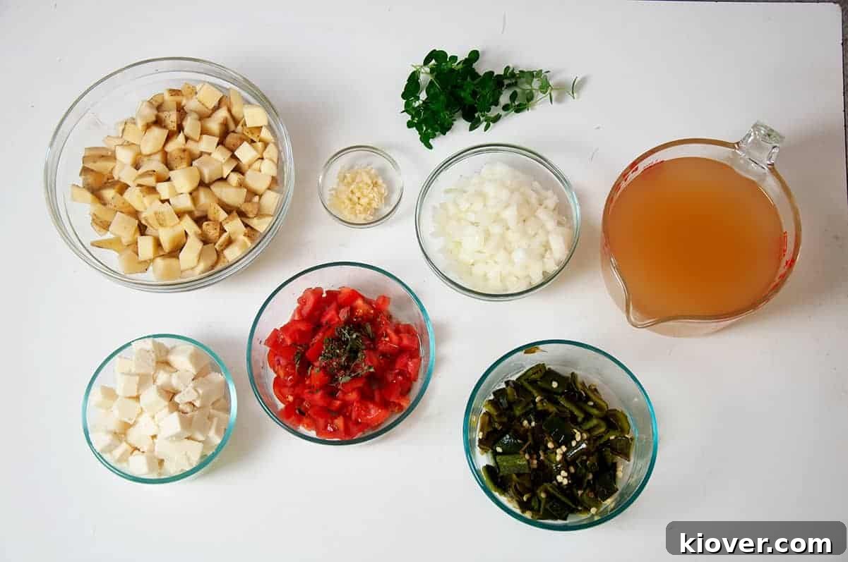 Many of the Ingredients for this soup including Queso Fresco, tomato, oregano, roasted poblano peppers, and chicken broth, artfully arranged on a rustic surface.