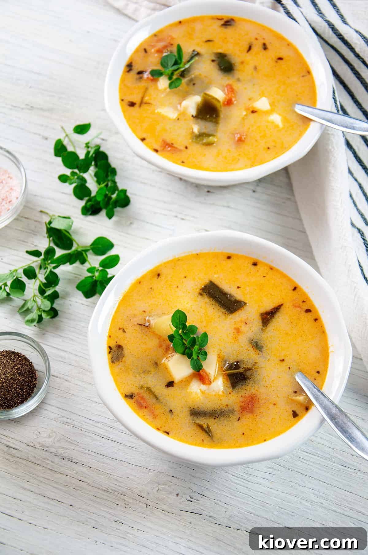 Two bowls of Caldo Queso on a white table with salt, pepper, and oregano, perfectly prepared and ready to serve.