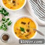 Two bowls of Caldo de Queso with oregano, pepper, and salt shown on the side.