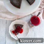 One slice of our Kladdkaka Swedish Sticky Cake on a white plate, covered in raspberry topping and a spoon to the side.