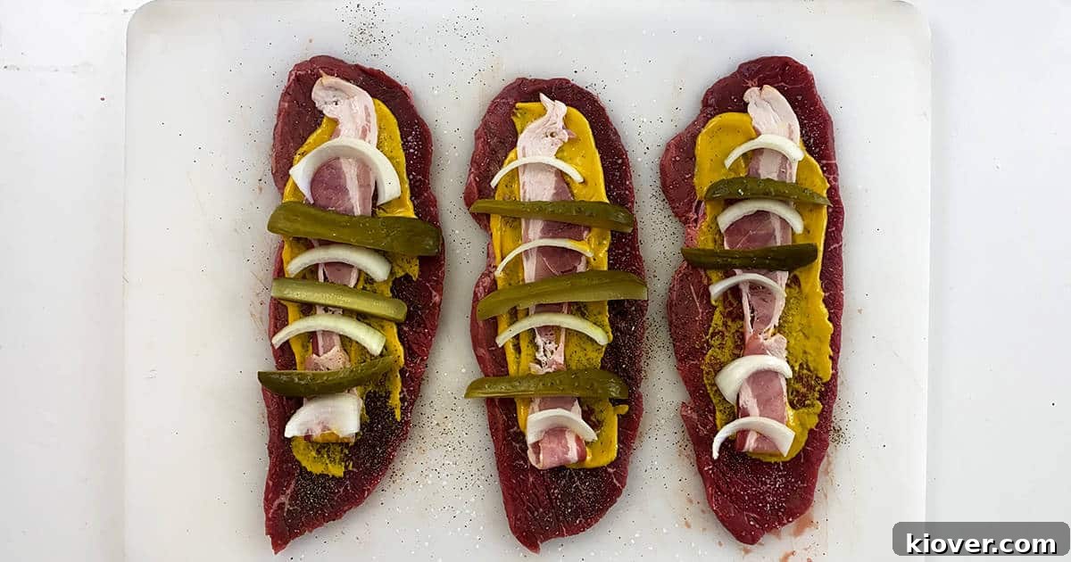Three slices of beef laid out with all of the rouladen ingredients on them.