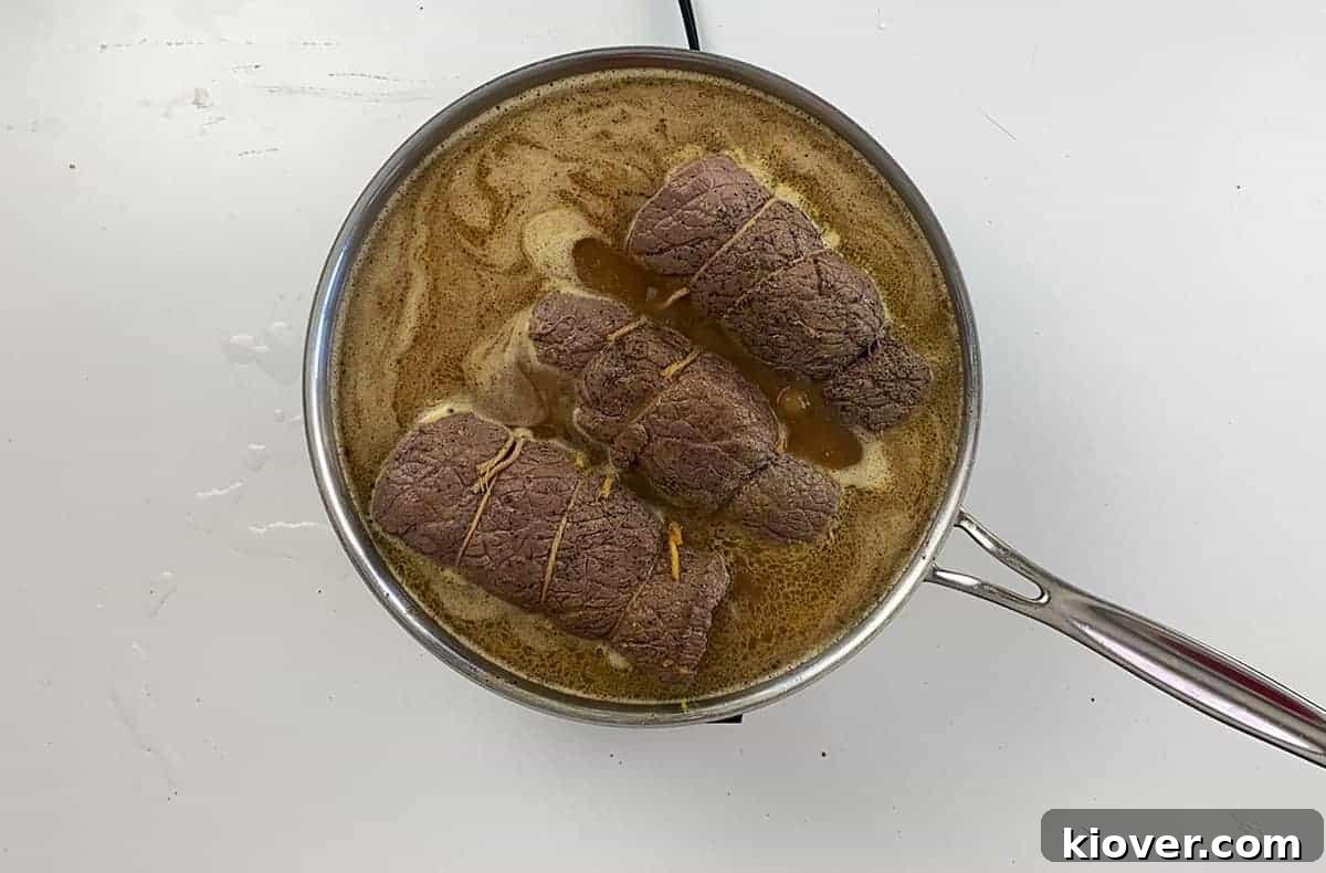 In large pan, three Rouladen are simmering in beef gravy.
